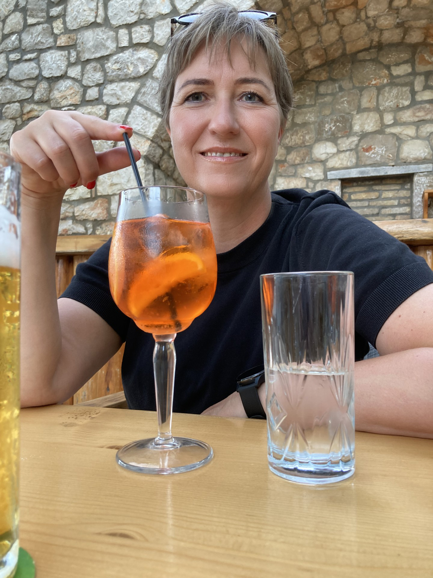 Bianca genießt Aperol Spritz in gemütlichem Restaurant mit Natursteinmauer – entspannter Urlaubsabend in Griechenland