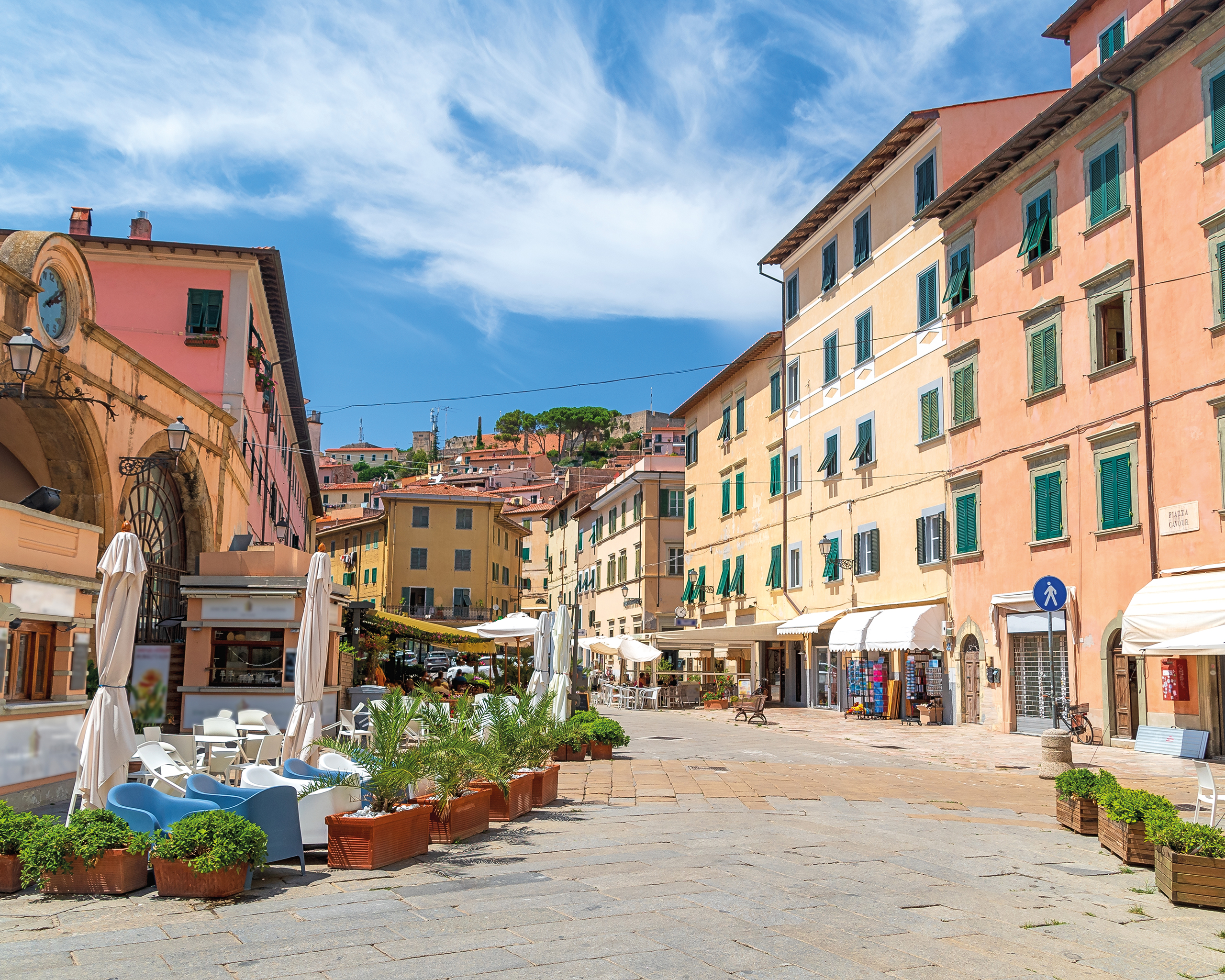 Pastellfarbene Häuser und kleine Cafés auf einer sonnigen Piazza in der Altstadt von Portoferraio auf der Insel Elba.