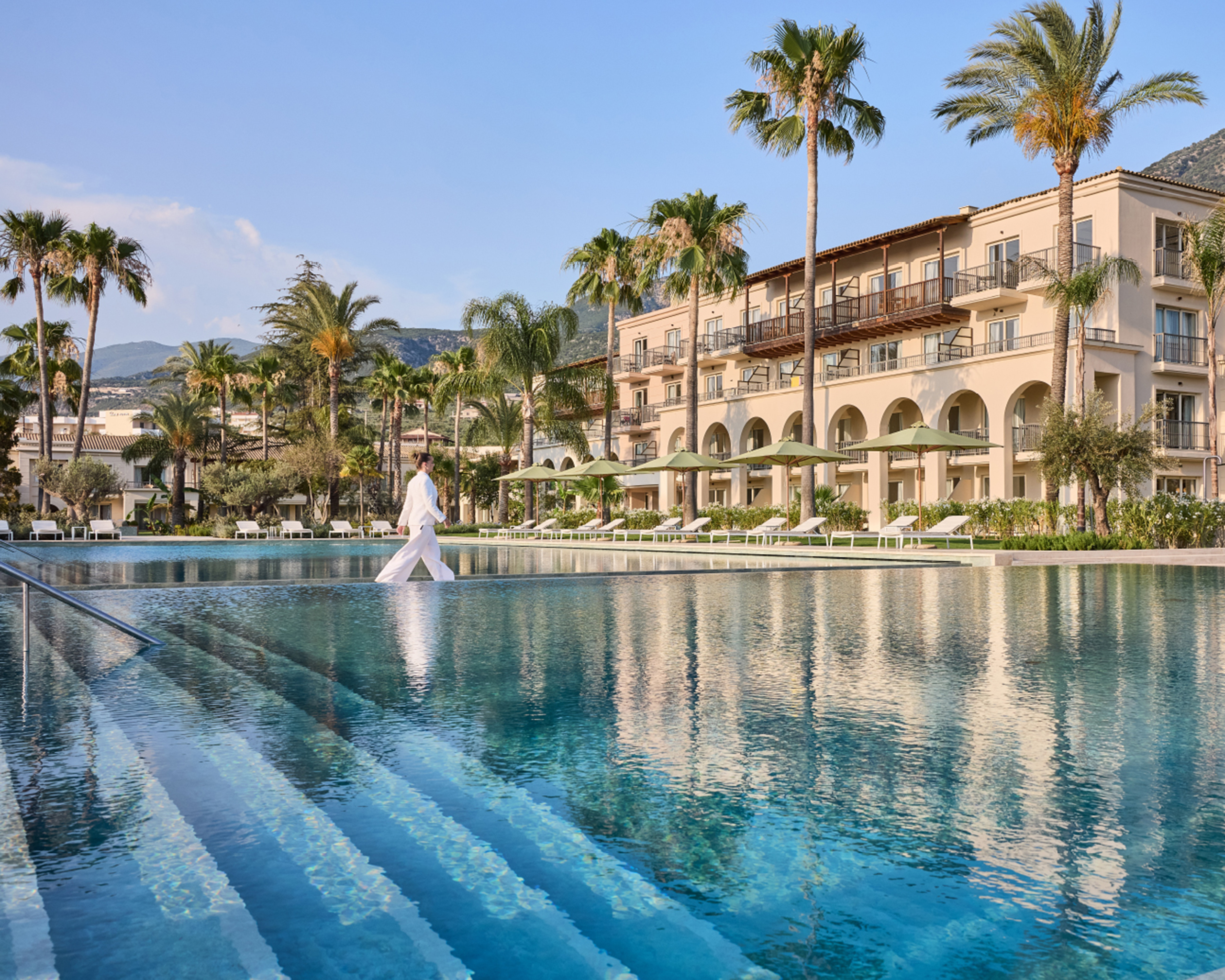Großer Außenpool des Grecotel Filoxenia Kalamata mit Palmen, Sonnenliegen und mediterranem Hotelgebäude im Hintergrund. © Grecotel Filoxenia Kalamata / Hotel