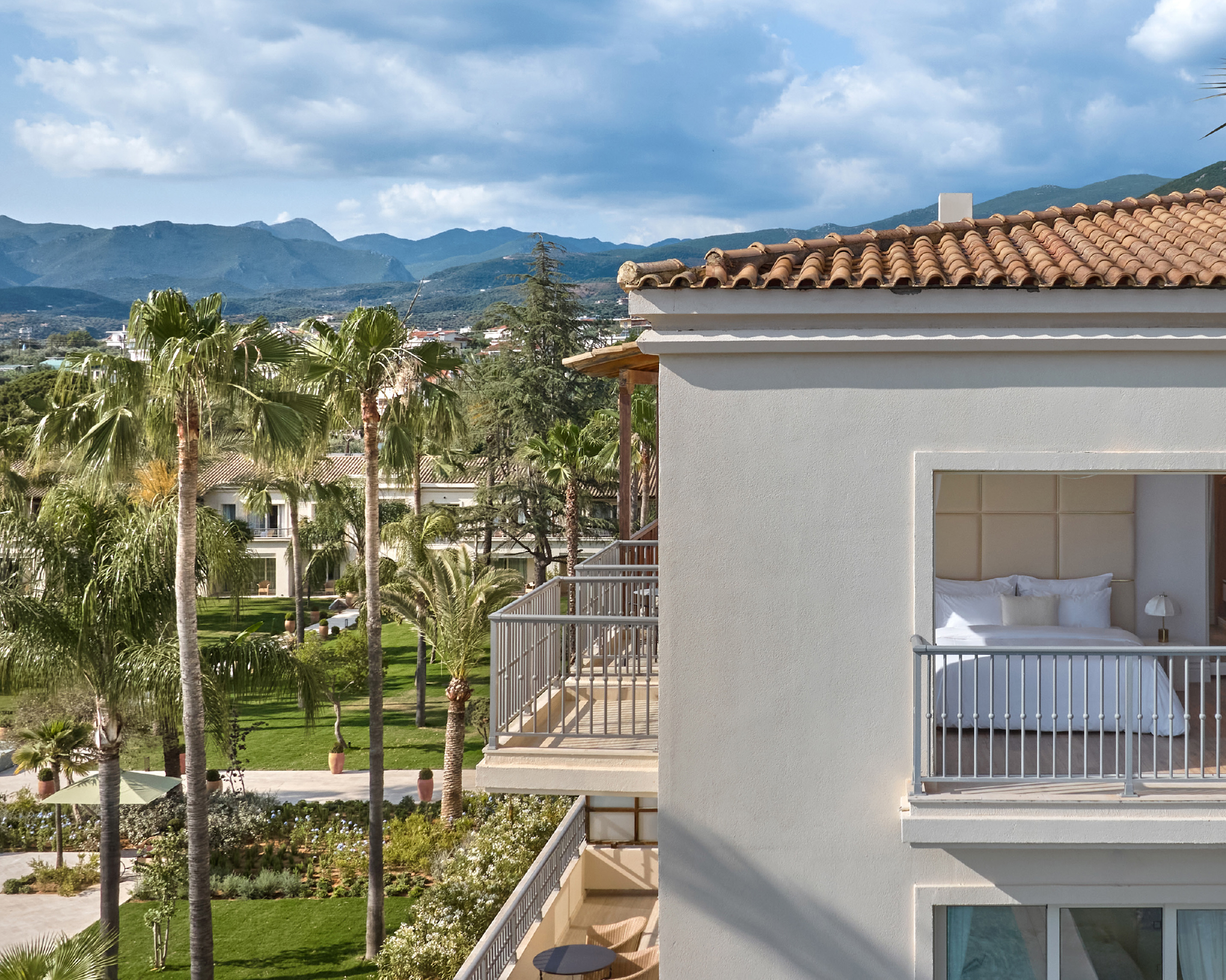 Blick auf die gepflegte Gartenanlage des Grecotel Filoxenia Kalamata mit Palmen, Hotelbalkon und Bergen im Hintergrund. © Grecotel Filoxenia Kalamata / Hotel