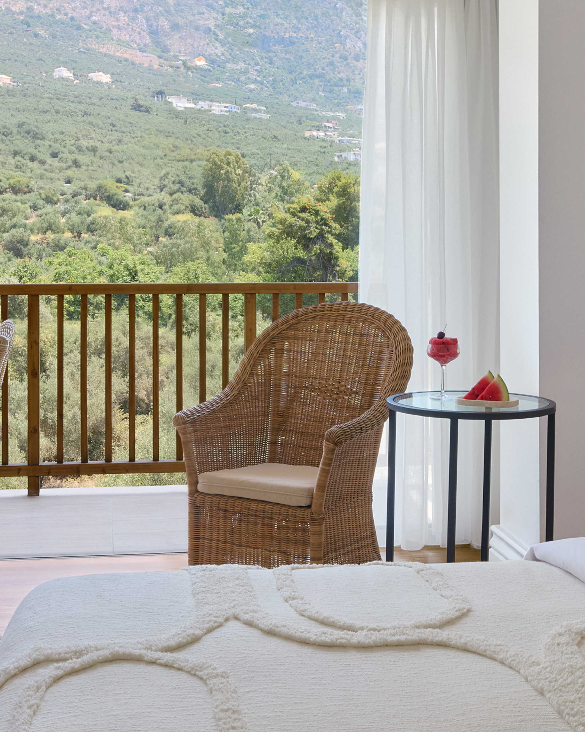 Superior Room im Grecotel Filoxenia Kalamata mit hellem Bett, Korbsessel und Balkon mit Blick auf die grüne Berglandschaft. © Grecotel Filoxenia Kalamata / Hotel