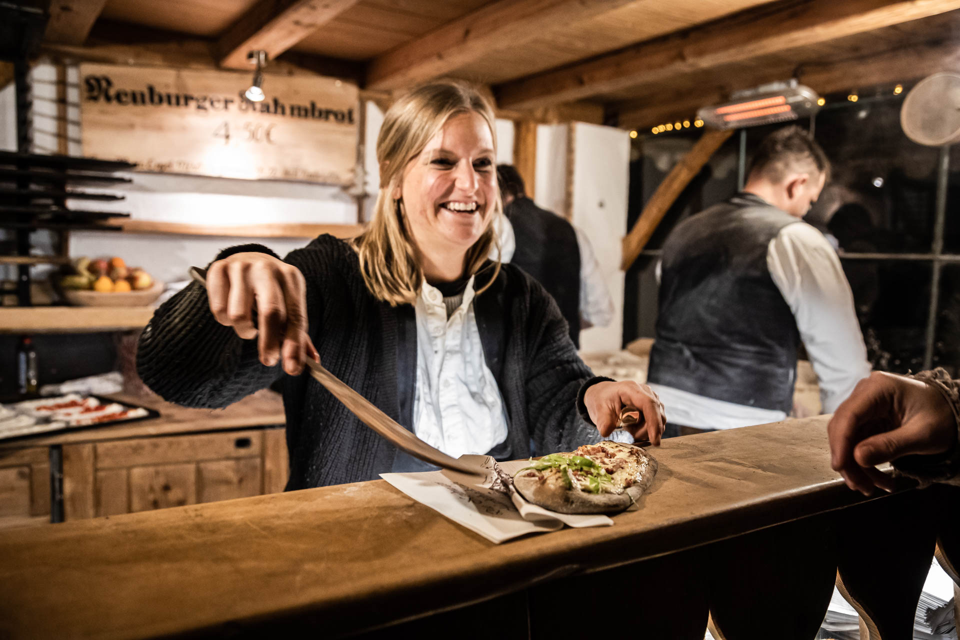 Lächelnde Marktfrau serviert frisch Gebackenes – winterliche Köstlichkeiten auf dem Bad Hindelang Weihnachtsmarkt.