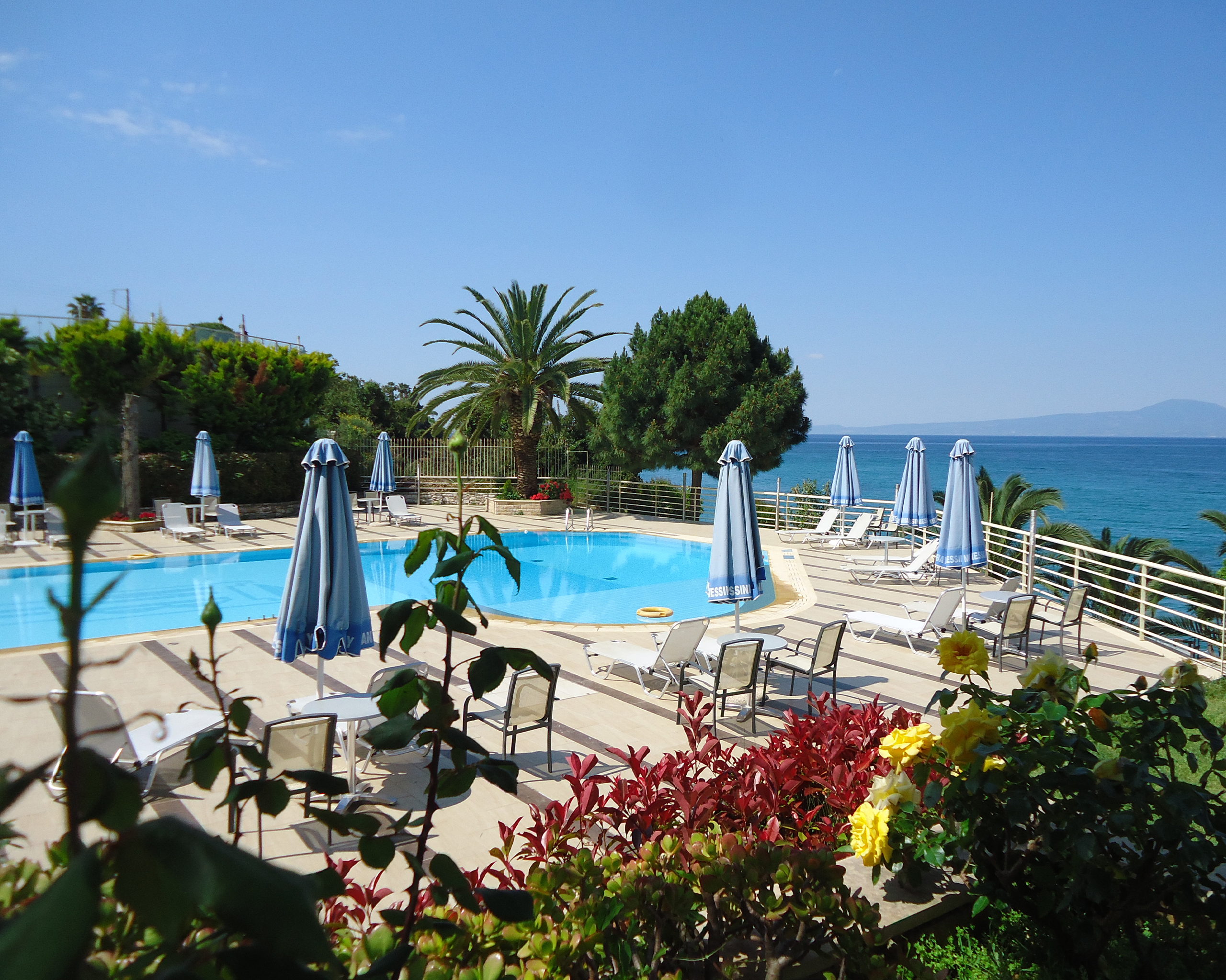 Großer Außenpool des Messinian Bay Hotels in Kalamata mit Liegestühlen, Sonnenschirmen und direktem Blick auf das Meer. © Idealtours