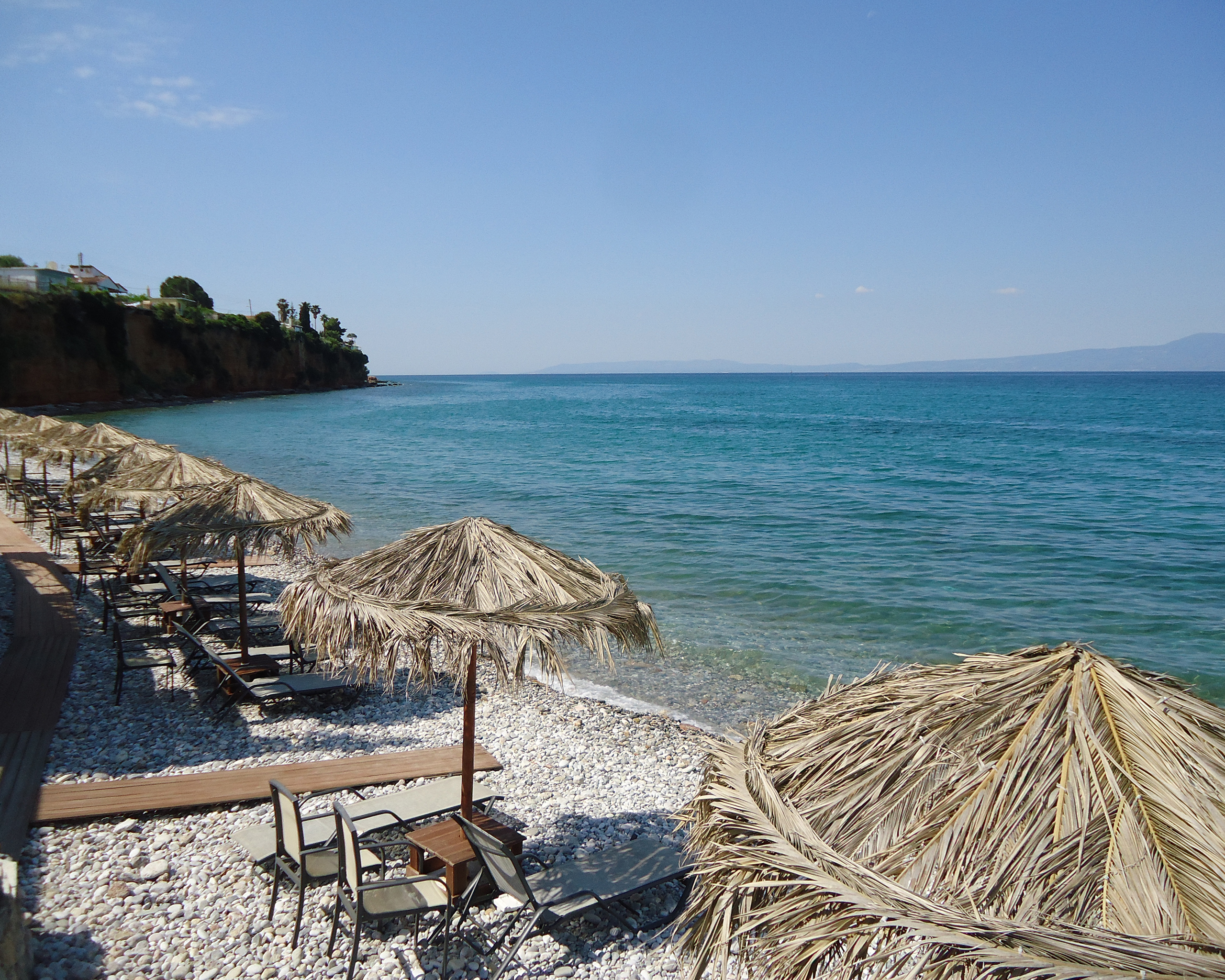 Steinstrand bei Kalamata mit Liegen und Strohschirmen direkt am klaren Meer, Messinian Bay Region, Griechenland. © Idealtours