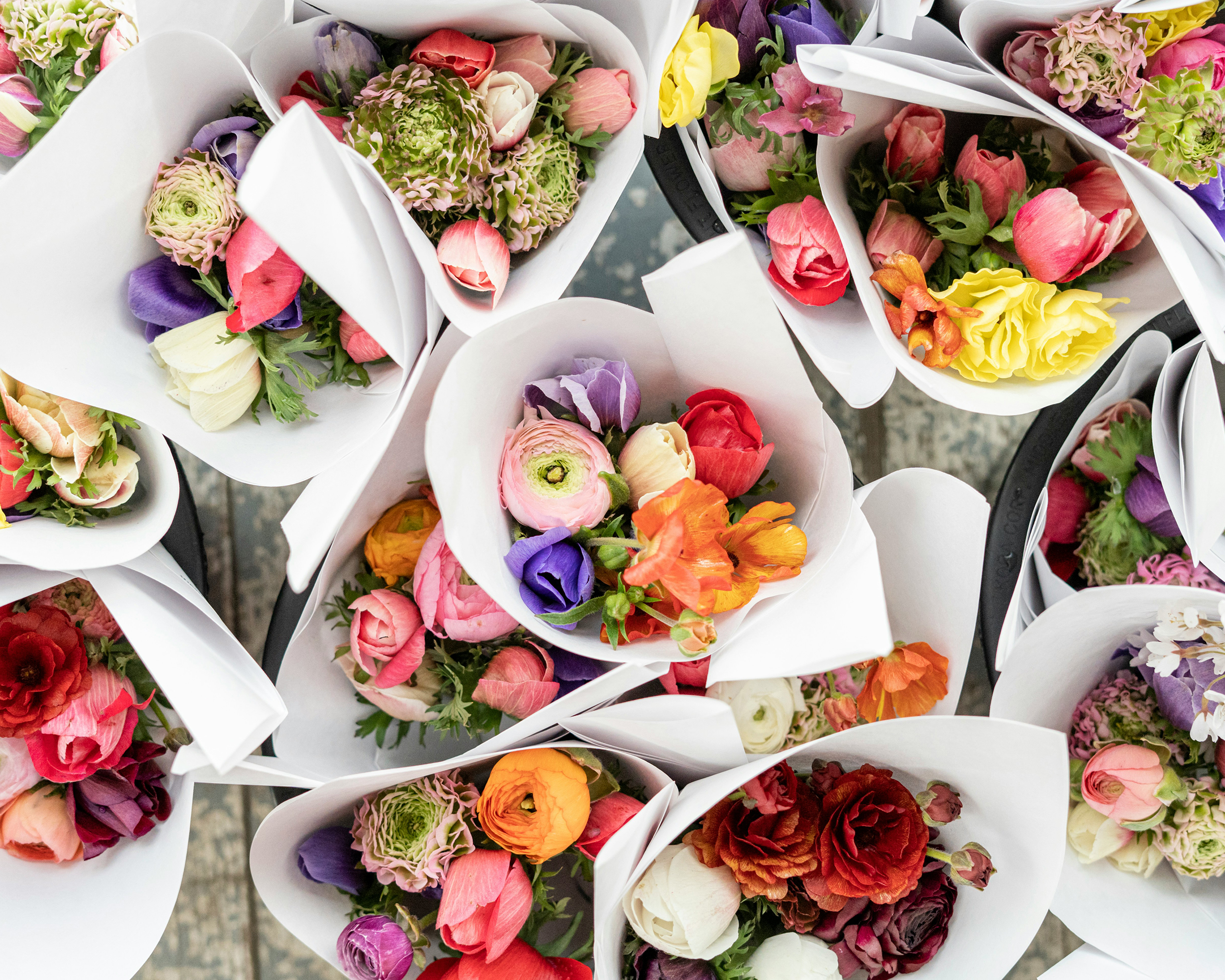 Bunte Blumensträuße in Papier gebunden, dicht an dicht arrangiert, als Symbol für Frühling, Freude und Muttertag.