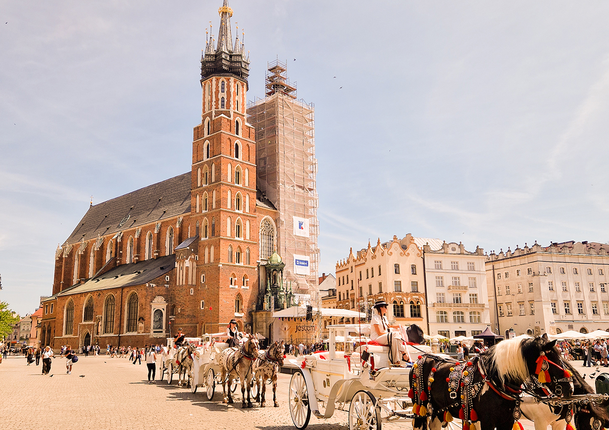 Krakauer Hauptmarkt mit Marienkirche und festlich geschmückten Pferdekutschen bei sonnigem Wetter.