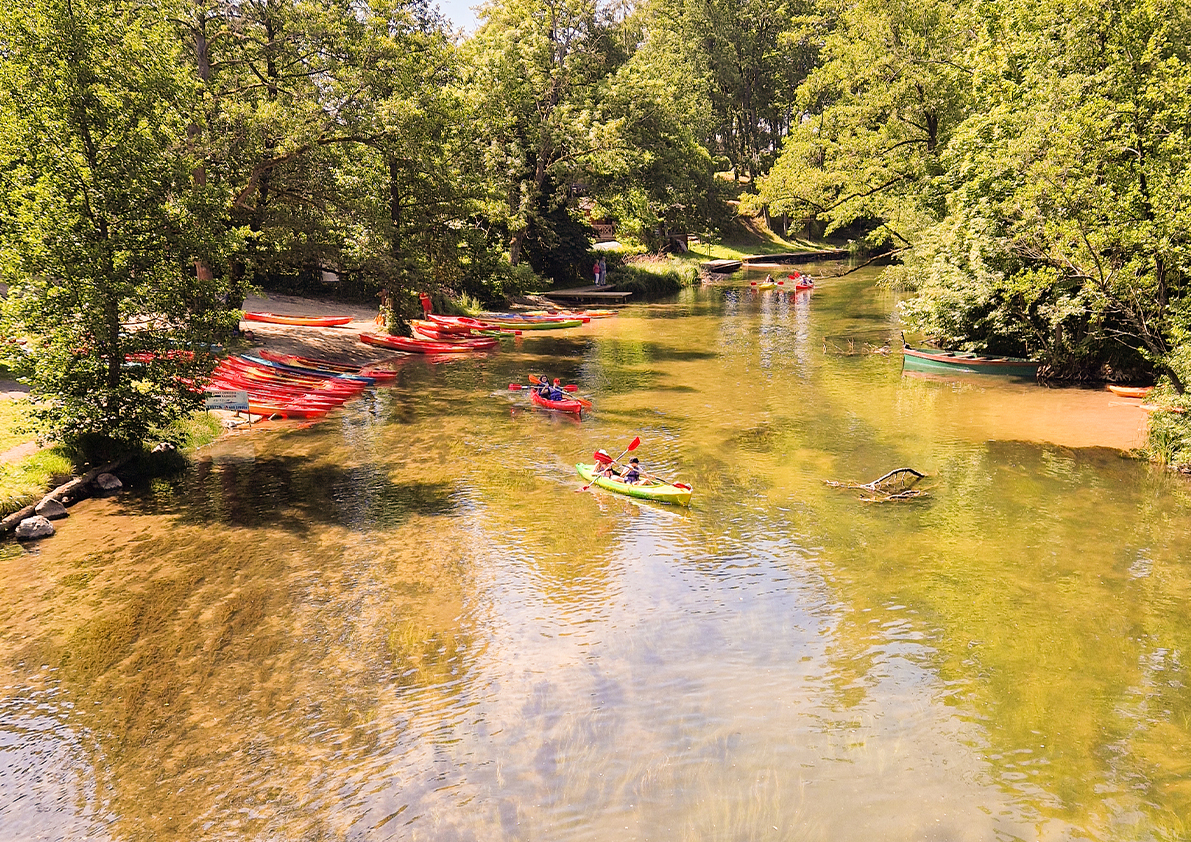 Kanufahrer auf einem ruhigen Fluss, umgeben von dichter grüner Natur in der Region Masuren.