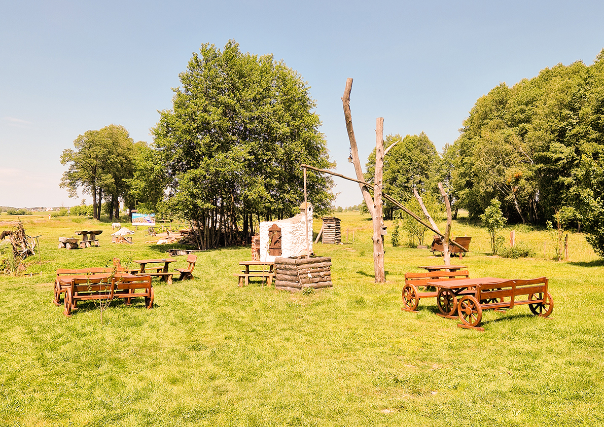 Rustikale Picknickwiese mit Holzbänken, Ziehbrunnen und weitläufiger Landschaft in Polen.