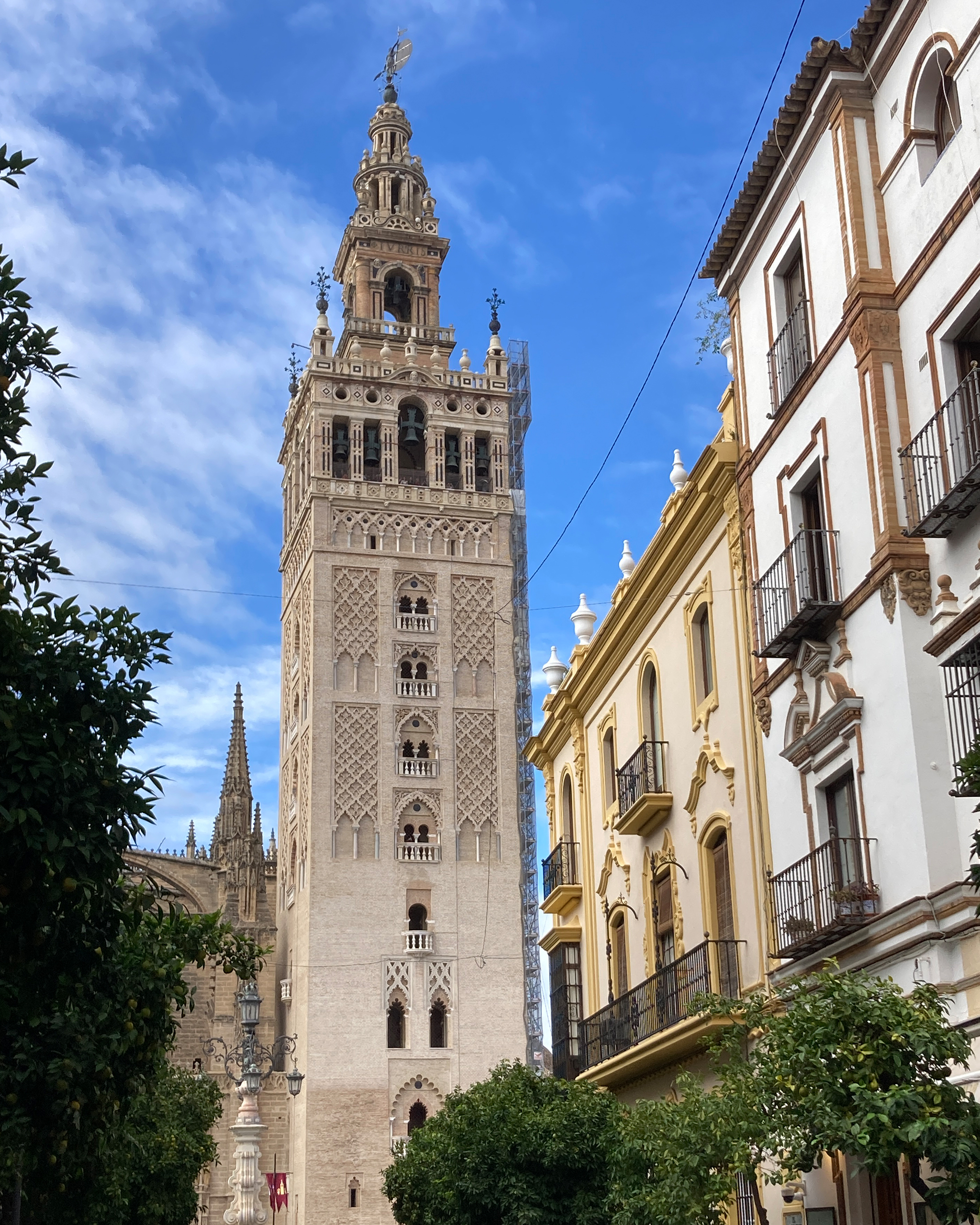 Die Giralda, der historische Glockenturm der Kathedrale von Sevilla, ragt zwischen traditionellen andalusischen Häuserfassaden in den blauen Himmel.
