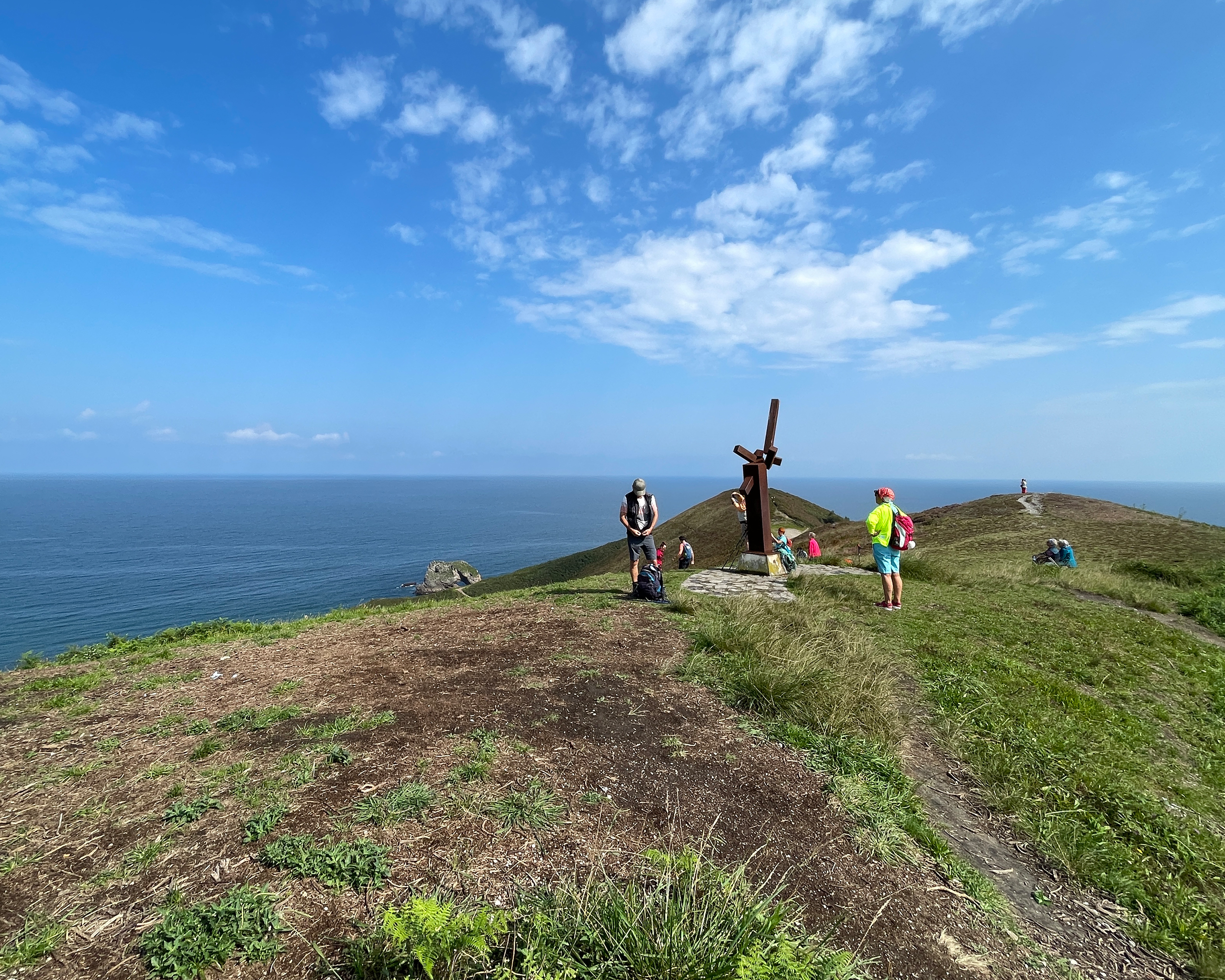 Pilger machen Rast an einem Holzkreuz auf einem grünen Hügel mit weitem Blick über den Atlantik entlang des Camino del Norte in Spanien.