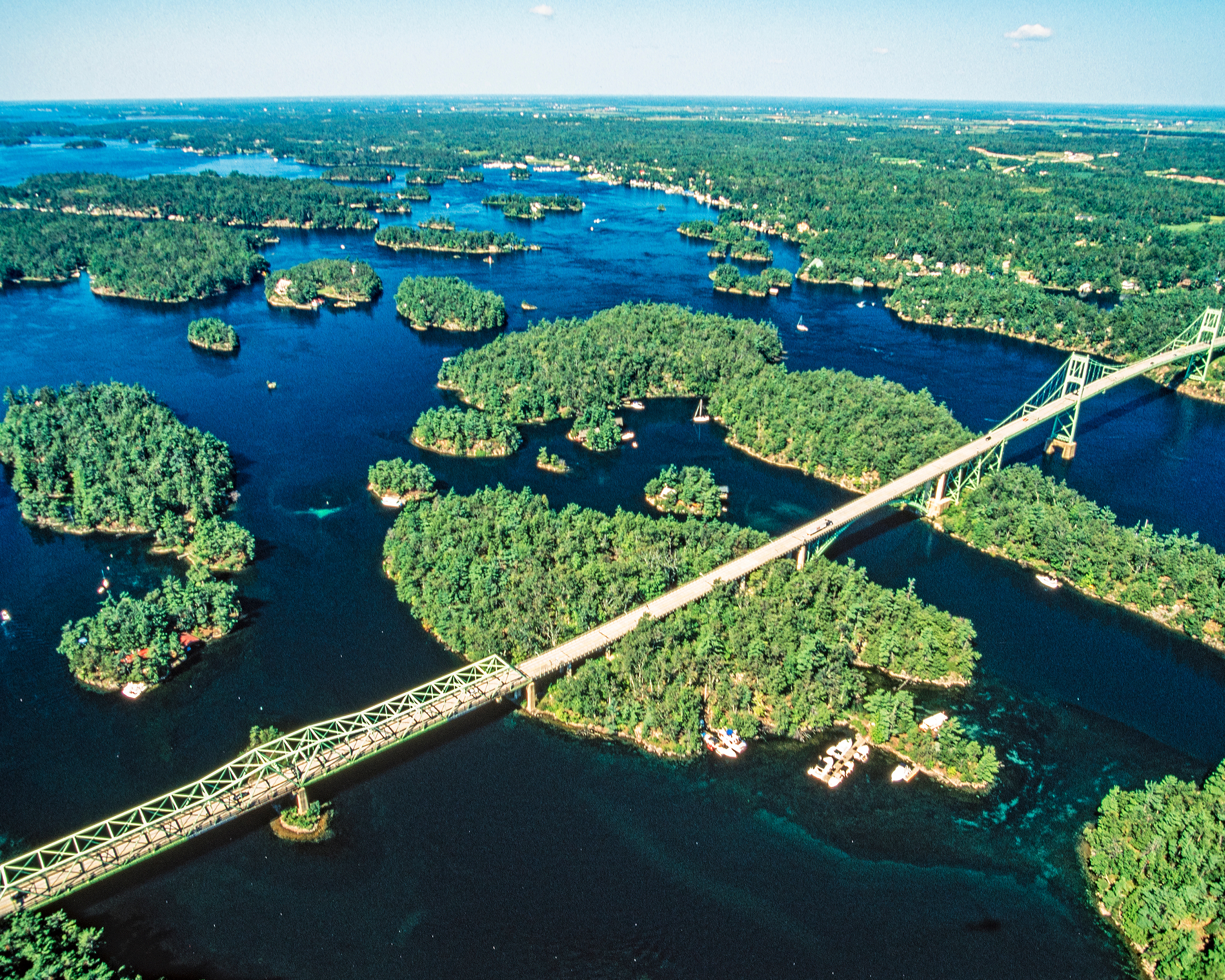 Luftaufnahme der Thousand Islands im Sankt-Lorenz-Strom mit zahlreichen bewaldeten Inseln und einer langen Brücke, die das Inselgebiet in Kanada verbindet.