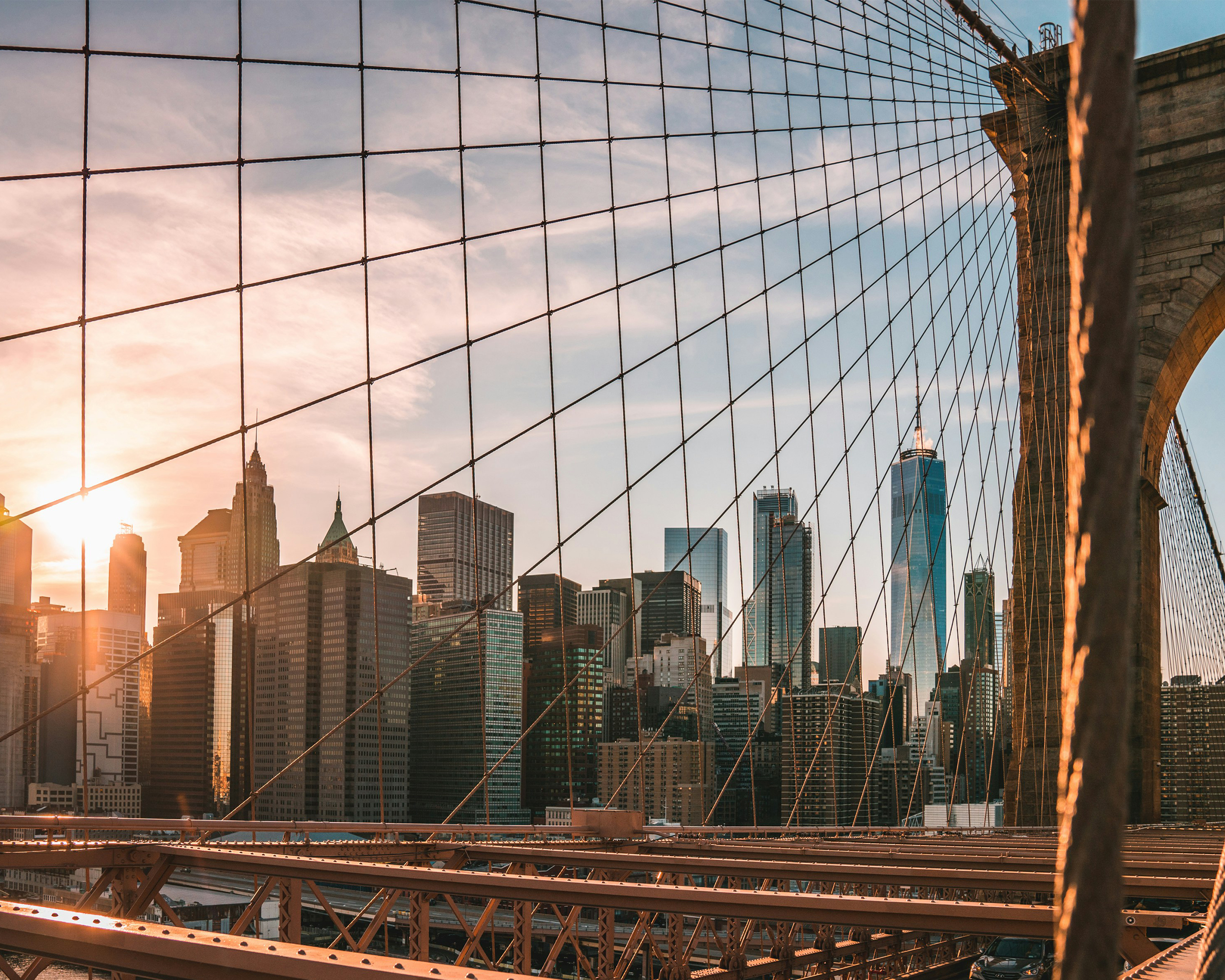 Blick von der Brooklyn Bridge auf die Skyline von Manhattan bei Sonnenuntergang mit Hochhäusern und warmem Abendlicht.