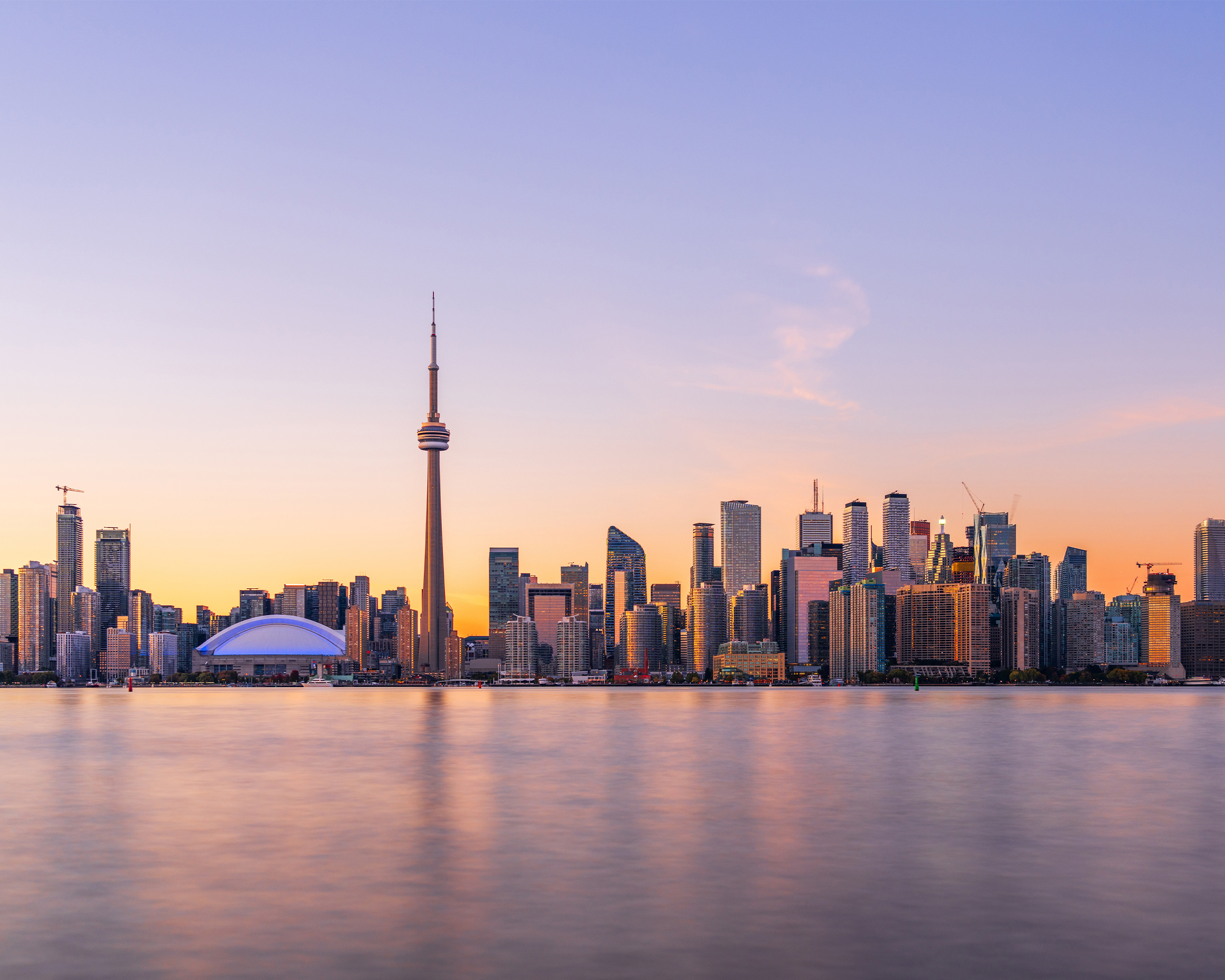 Skyline von Toronto mit dem CN Tower bei Sonnenuntergang, gespiegelt im ruhigen Wasser des Ontariosees.