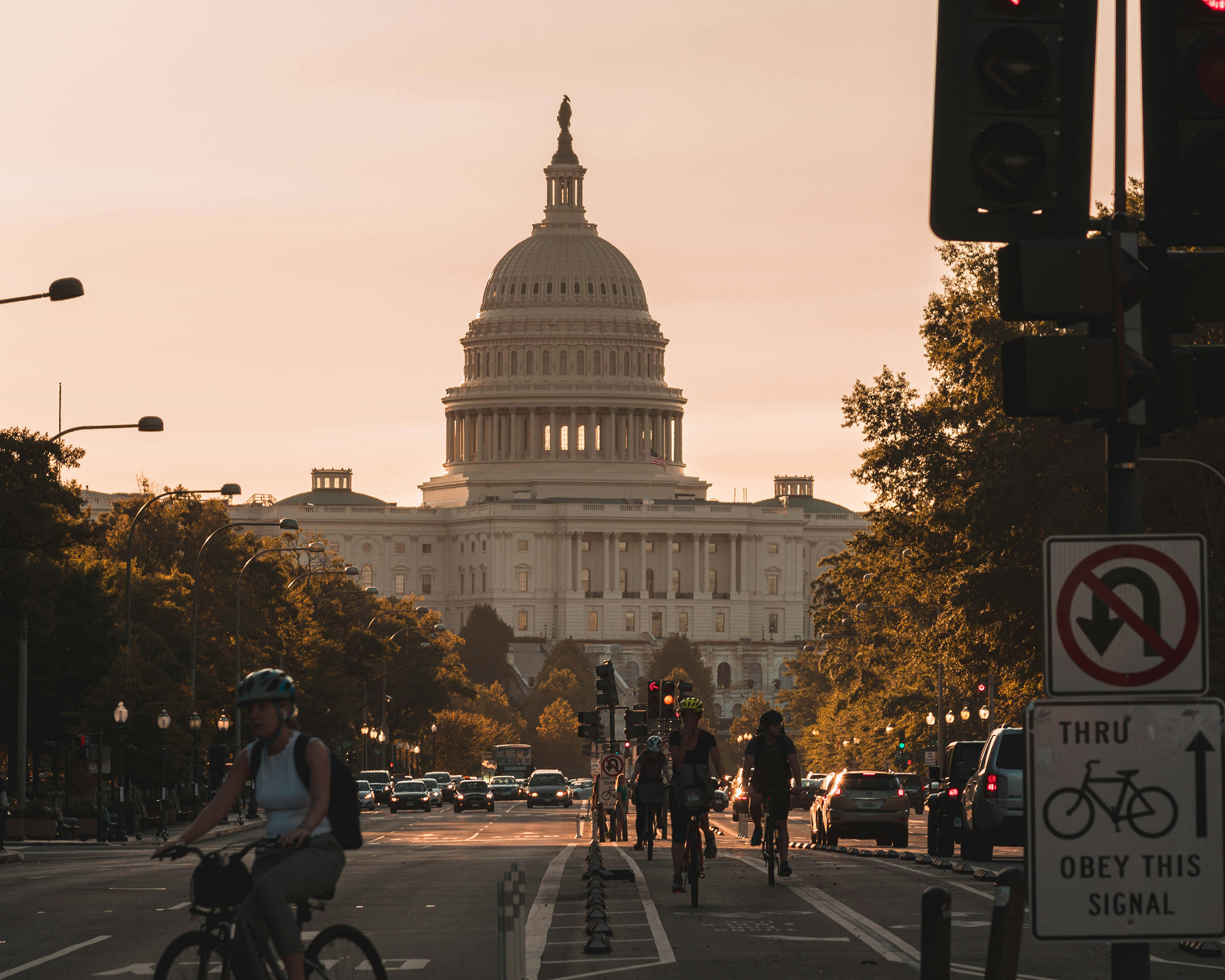 Das Kapitol in Washington D.C. im warmen Abendlicht, mit Radfahrern und Autos auf der breiten Avenue im Vordergrund.