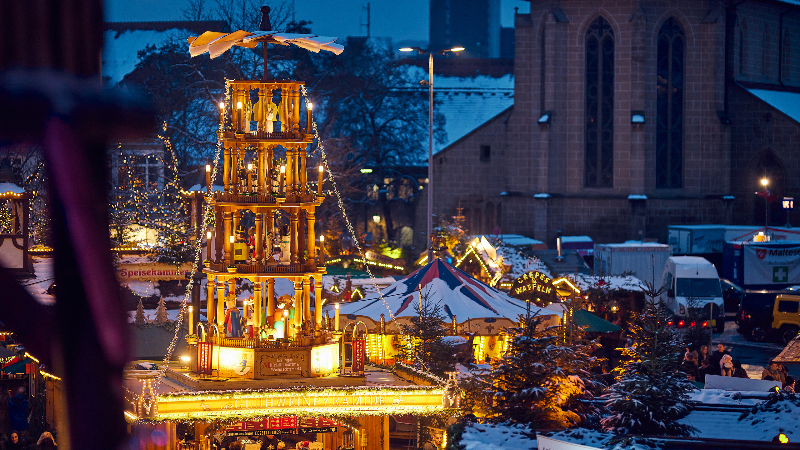 Leuchtende Pyramide auf dem Esslinger Mittelaltermarkt & Weihnachtsmarkt, umgeben von festlich geschmückten Ständen und dem historischen Dominikanerkloster im Hintergrund.