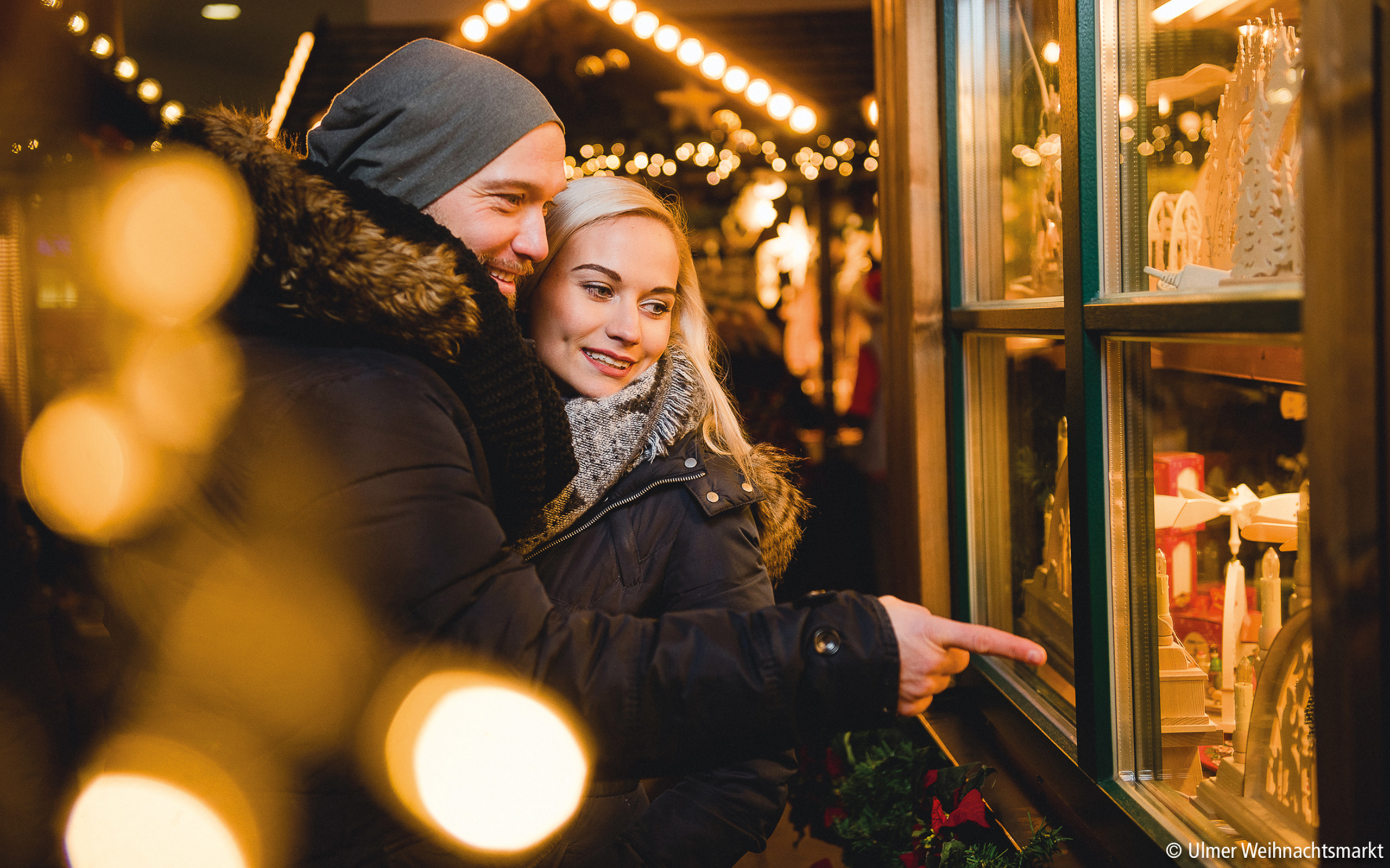 Glückliches Paar beim Bummeln und Schauen an festlich beleuchteten Ständen des Ulmer Weihnachtsmarkts