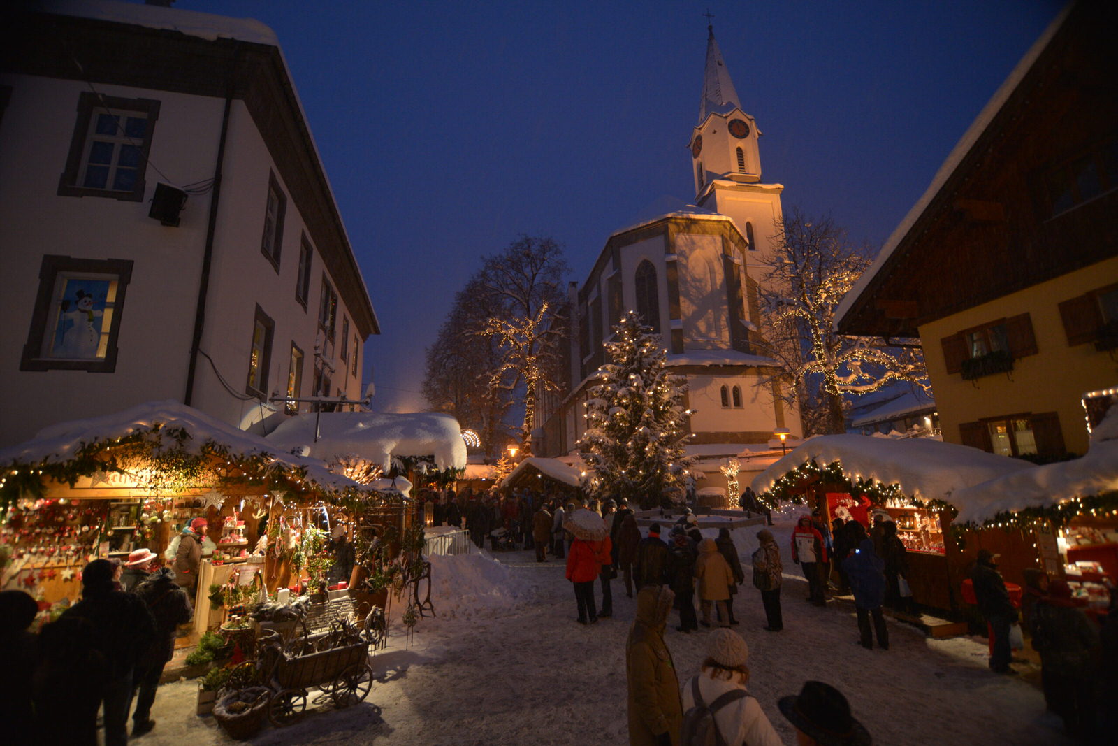 Winterlicher Weihnachtsmarkt in Bad Hindelang mit funkelnden Lichtern, festlich geschmückten Ständen und der Kirche im Hintergrund