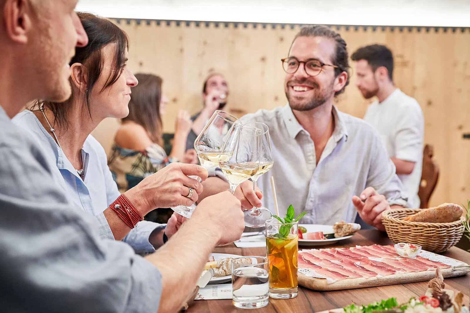 Gäste stoßen bei einer Weinverkostung mit Weißwein an und genießen Südtiroler Speck und Brot