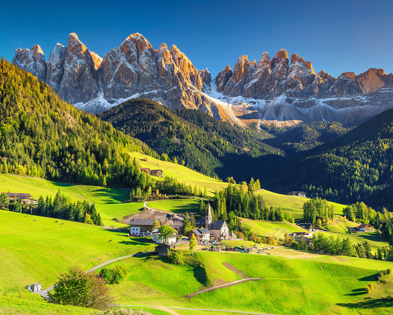 Grüne Almwiesen und Bergdorf vor den schroffen Gipfeln der Südtiroler Dolomiten