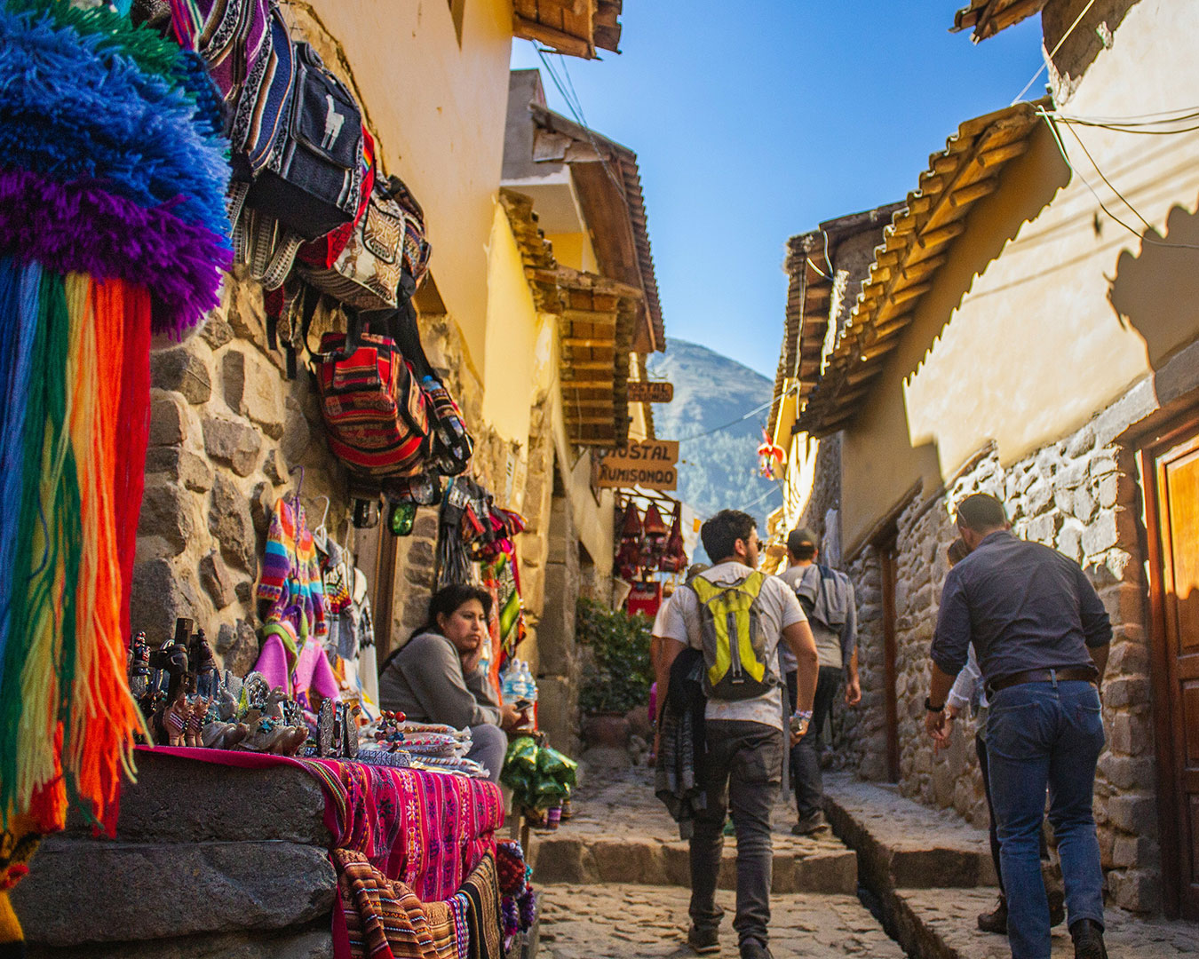 Enge Kopfsteingasse in Cusco, Peru, mit traditionellen Steinhäusern, bunten Andentextilien und Besuchern.
