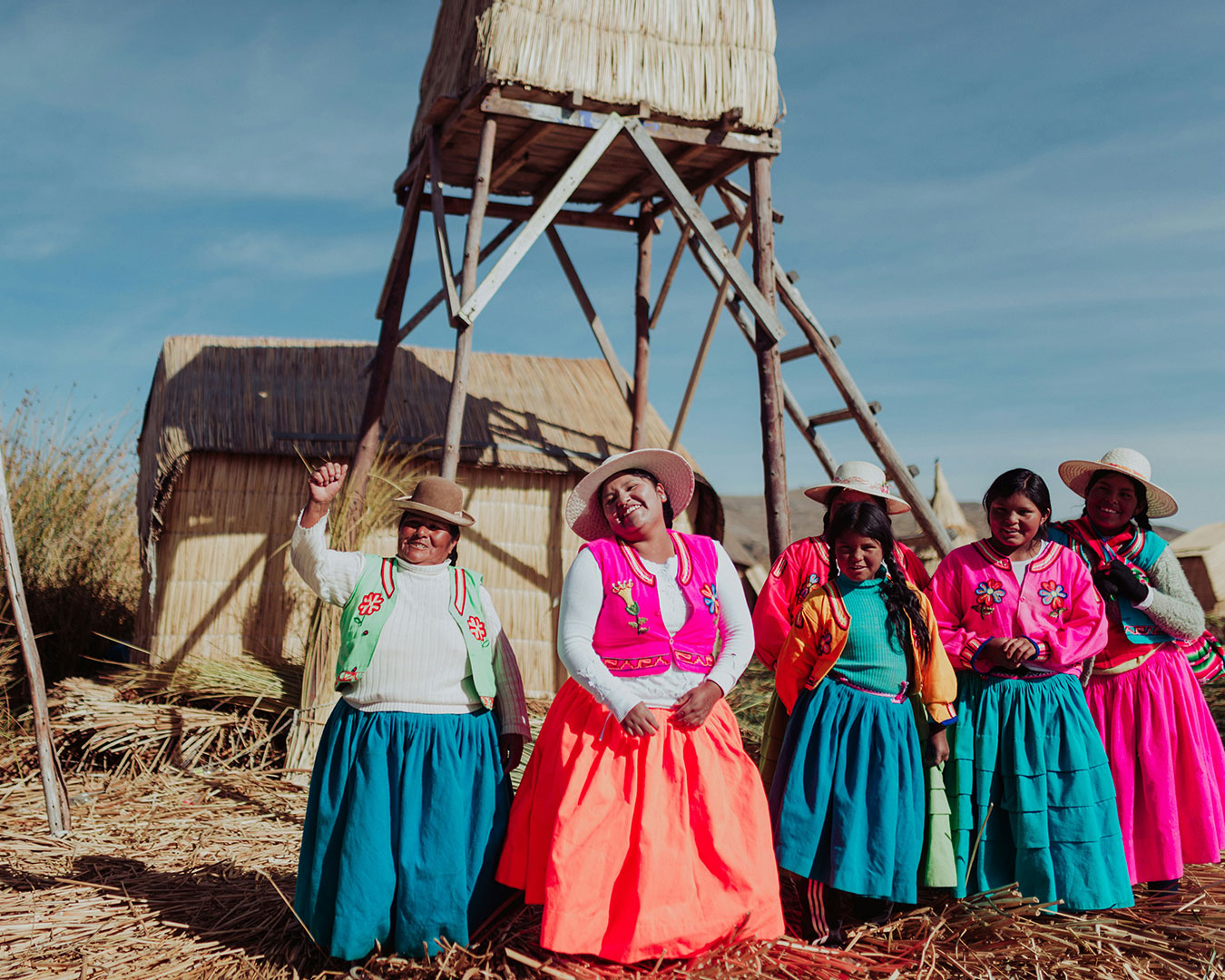 Frauen und Mädchen in farbenfroher traditioneller Kleidung auf den schwimmenden Uros-Inseln im Titicacasee in Peru, umgeben von Schilfhäusern.