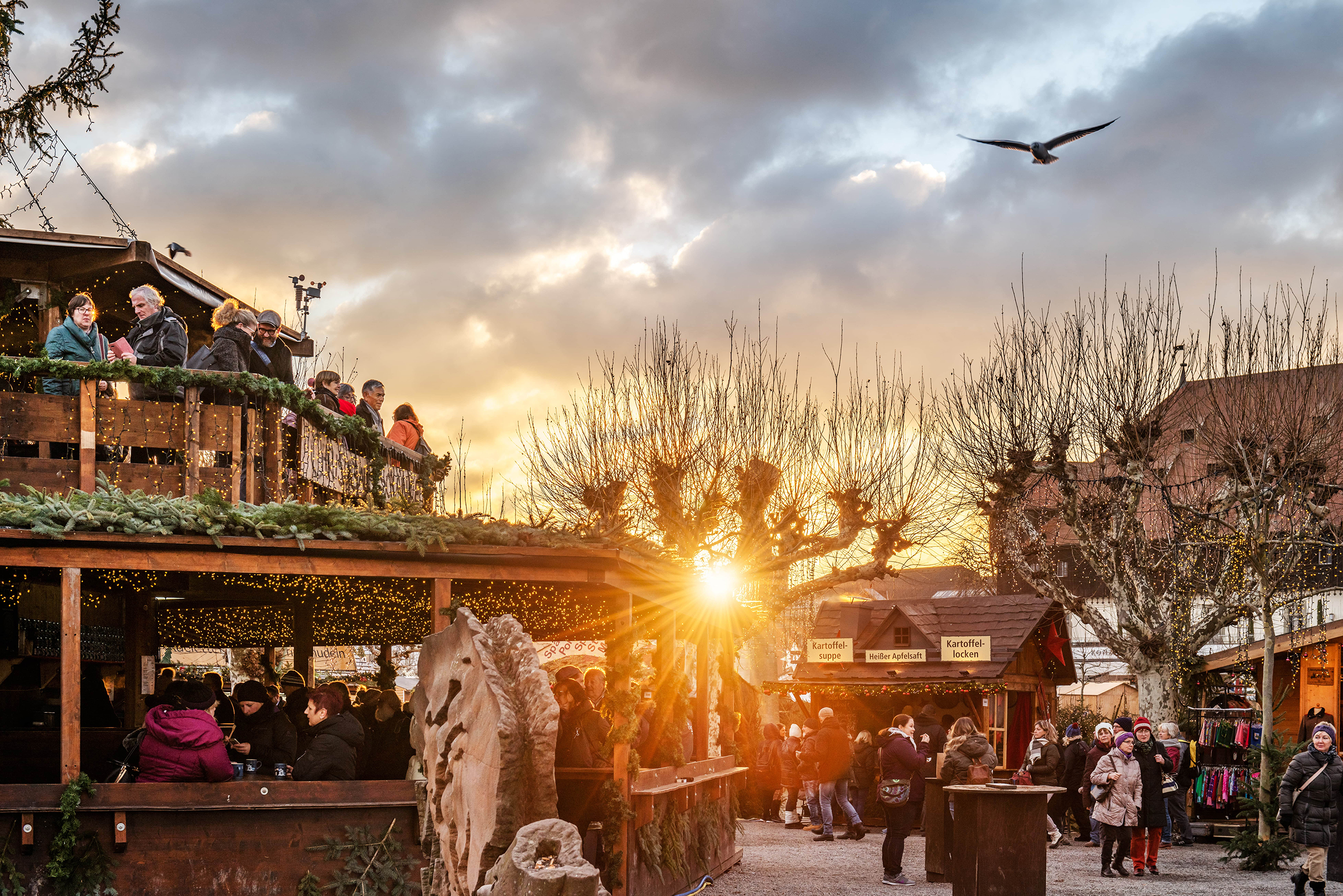 Stimmungsvoller Weihnachtsmarkt in Konstanz bei Sonnenuntergang – festlich geschmückte Hütten, gemütliche Menschenrunden und winterliche Abendromantik am Bodensee