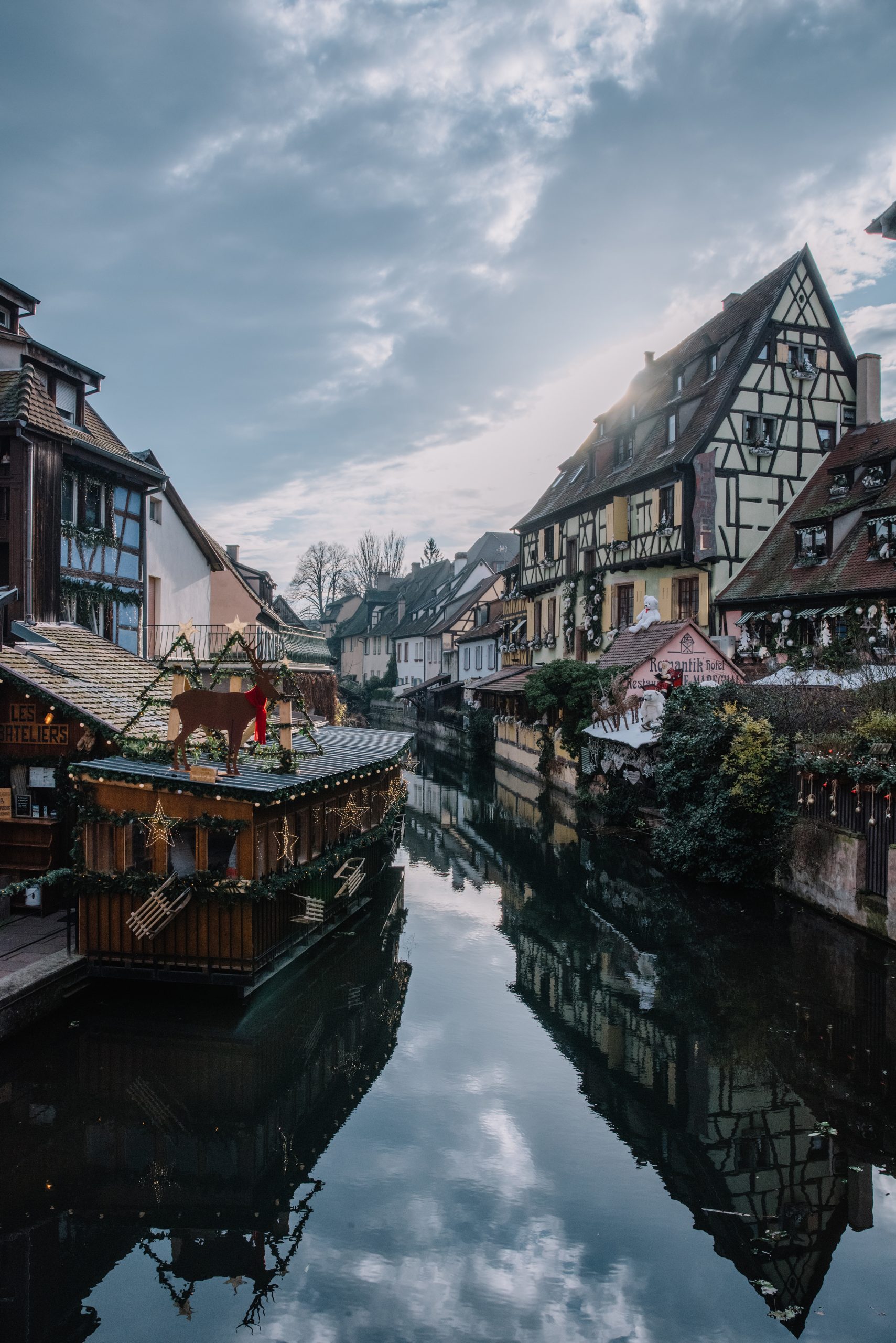 Colmars Fachwerkhäuser und weihnachtlich geschmückte Marktstände spiegeln sich im ruhigen Wasserkanal der Altstadt