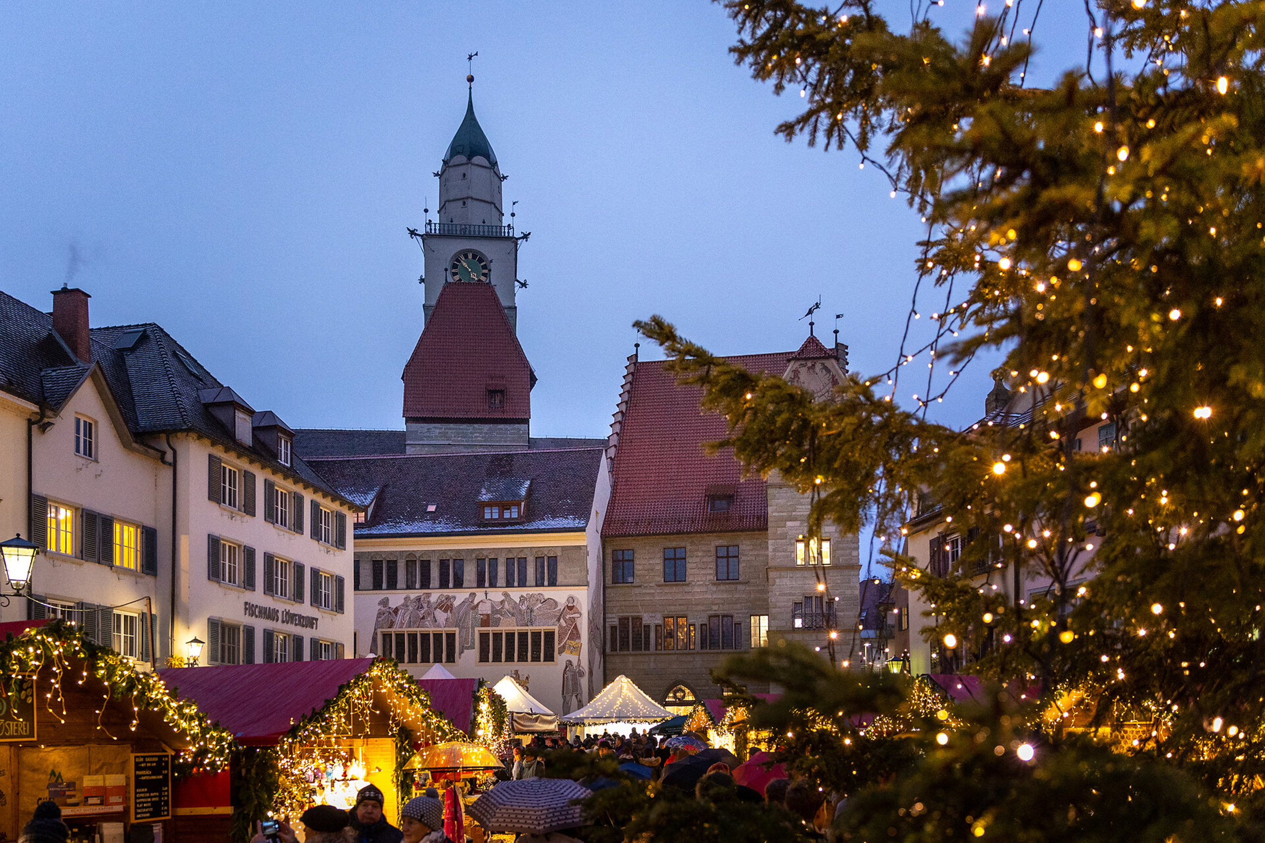Stimmungsvoller Weihnachtsmarkt in Überlingen am Bodensee mit festlich beleuchteten Hütten, dem imposanten Turm im Hintergrund und Lichterglanz im großen Weihnachtsbaum