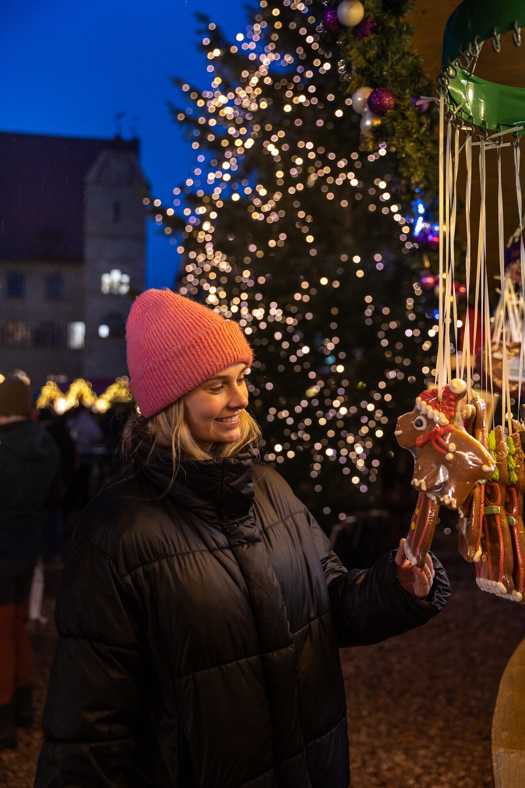 Junge Frau mit rosa Mütze betrachtet ein Lebkuchenherz in Rentierform am stimmungsvoll dekorierten Stand des Überlinger Weihnachtsmarktes