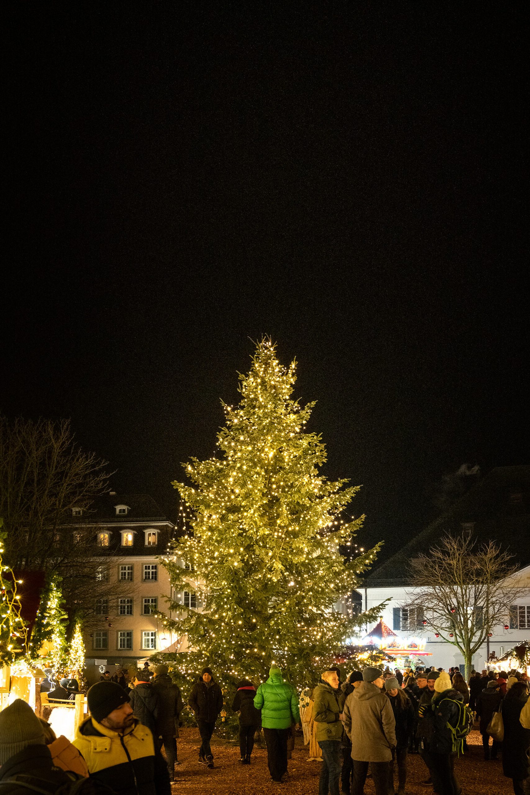 Beeindruckender Weihnachtsbaum mit hunderten Lichtern erhellt den Platz des Überlinger Weihnachtsmarktes, umgeben von Besuchern in winterlicher Atmosphäre